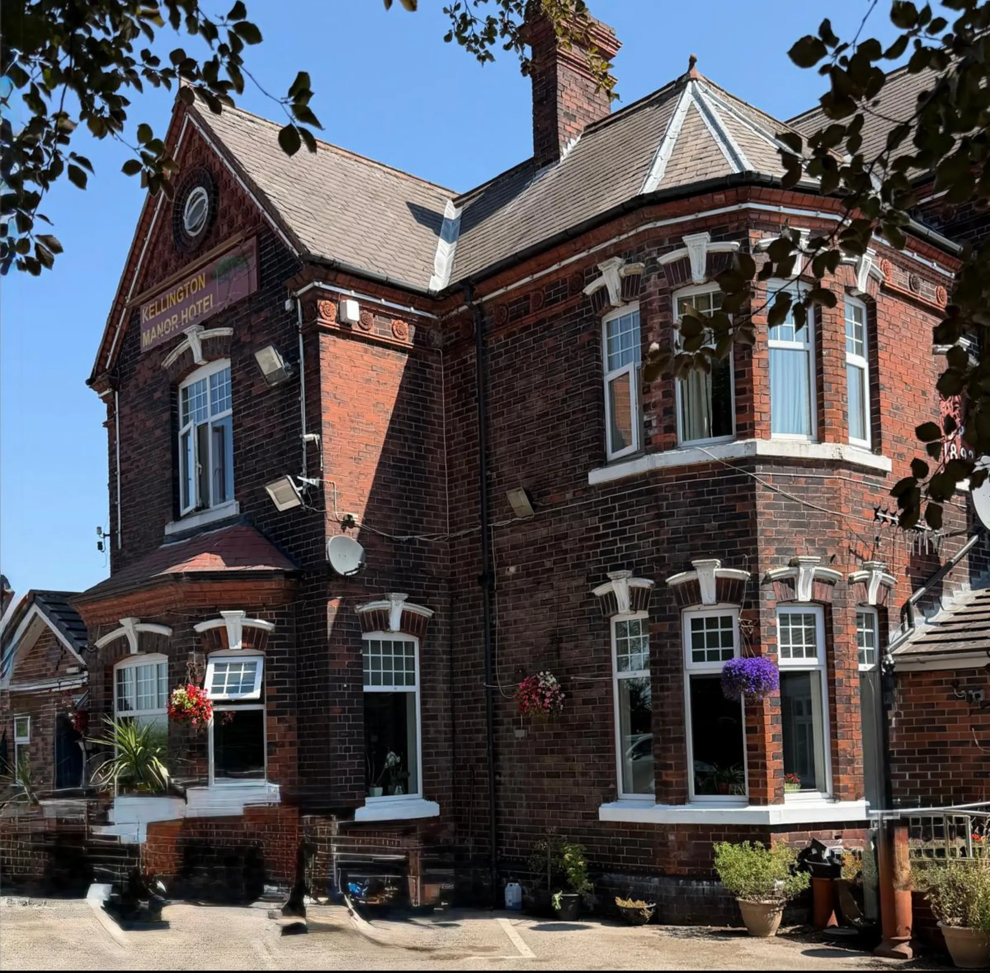 Kellington Manor's red-brick 1892 house, framed by trees on a bright day